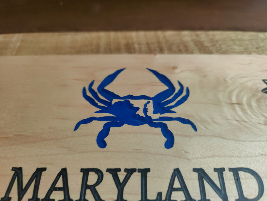 Close-up of a light wood surface with a blue crab logo above the word 'MARYLAND' in dark lettering.
