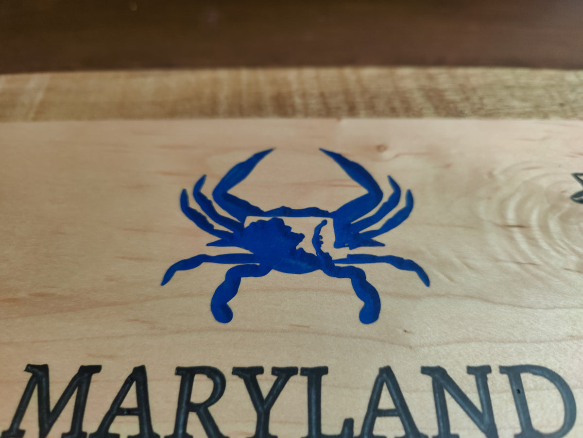 Close-up of a light wood surface with a blue crab logo above the word 'MARYLAND' in dark lettering.
