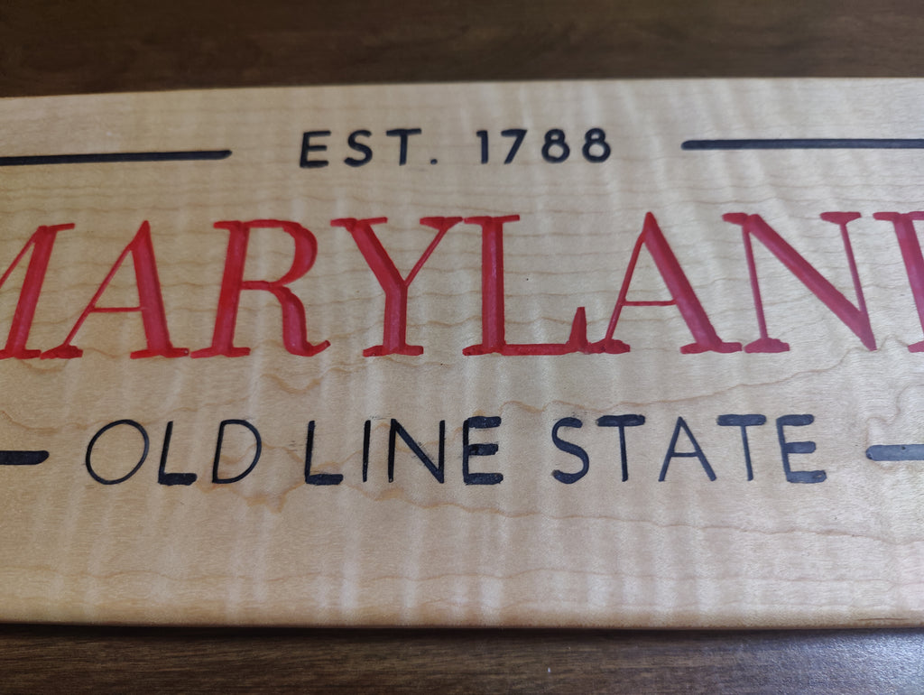 A close-up of a light natural wood sign featuring the text 'EST. 1788' and 'MARYLAND OLD LINE STATE' in red and black lettering.