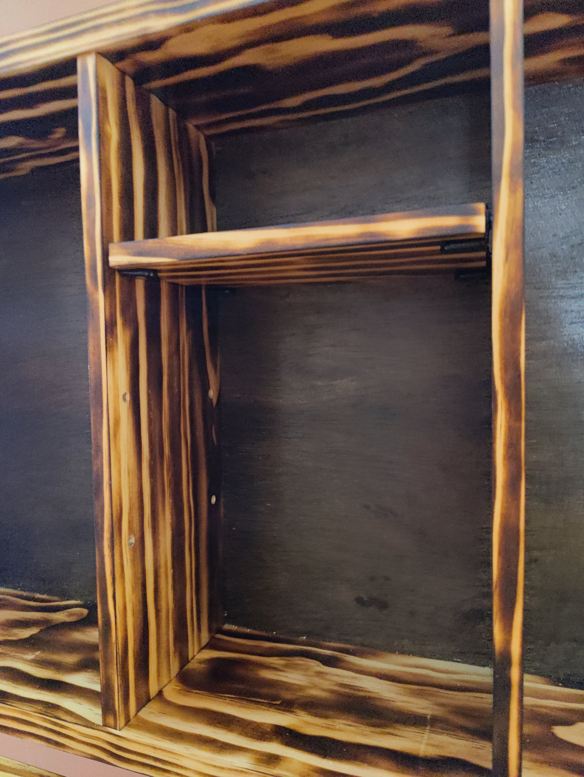 Close-up of a wooden shelving unit or cabinet interior with a single shelf, featuring a dark brown finish with prominent charred or burned wood grain patterns.