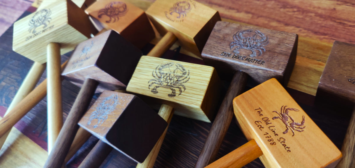 A group of wooden mallets with engraved crab designs and text, displayed on a dark wooden surface.