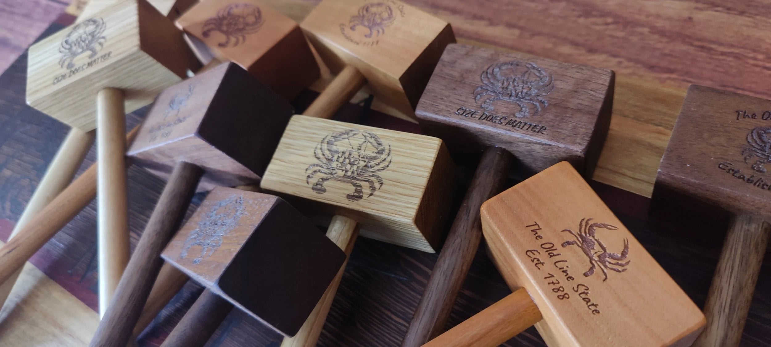 A group of wooden crab mallet-style tools or hammers with engraved crab illustrations and text, arranged on a wooden surface.