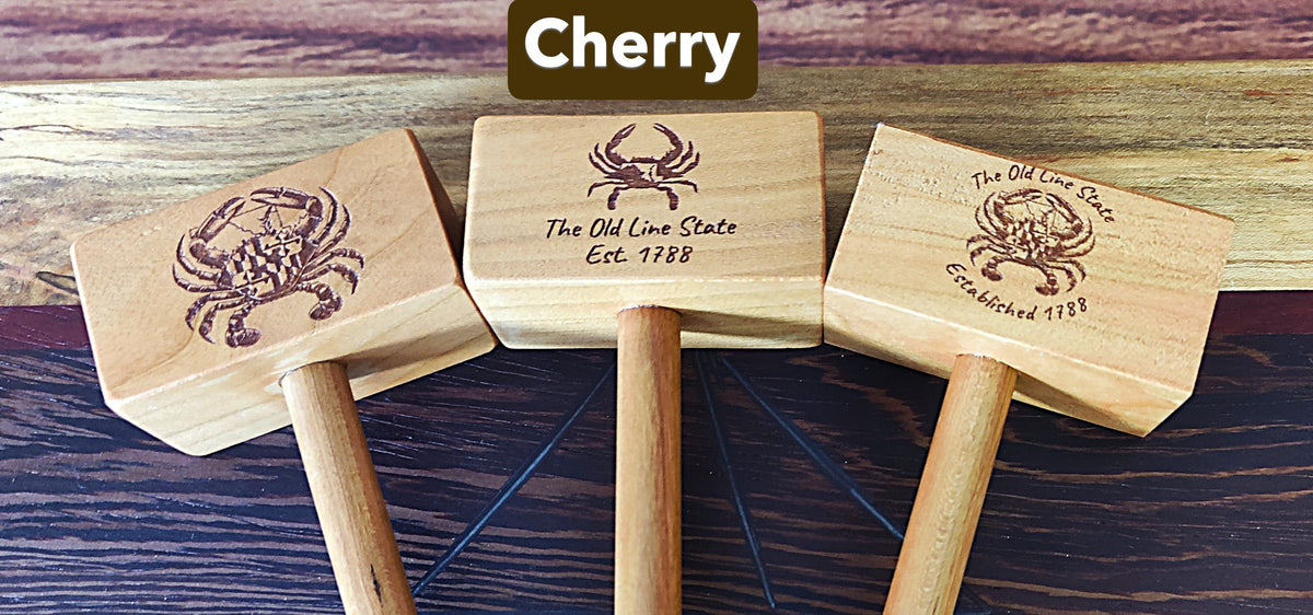 Three wooden mallets with crab engravings are arranged on a dark wood surface. A brown label at the top reads 'Cherry'.