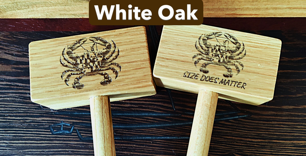 Two small wooden mallets labeled 'White Oak' with engraved crab designs and one reading 'SIZE DOES MATTER,' shown on a dark wood surface.
