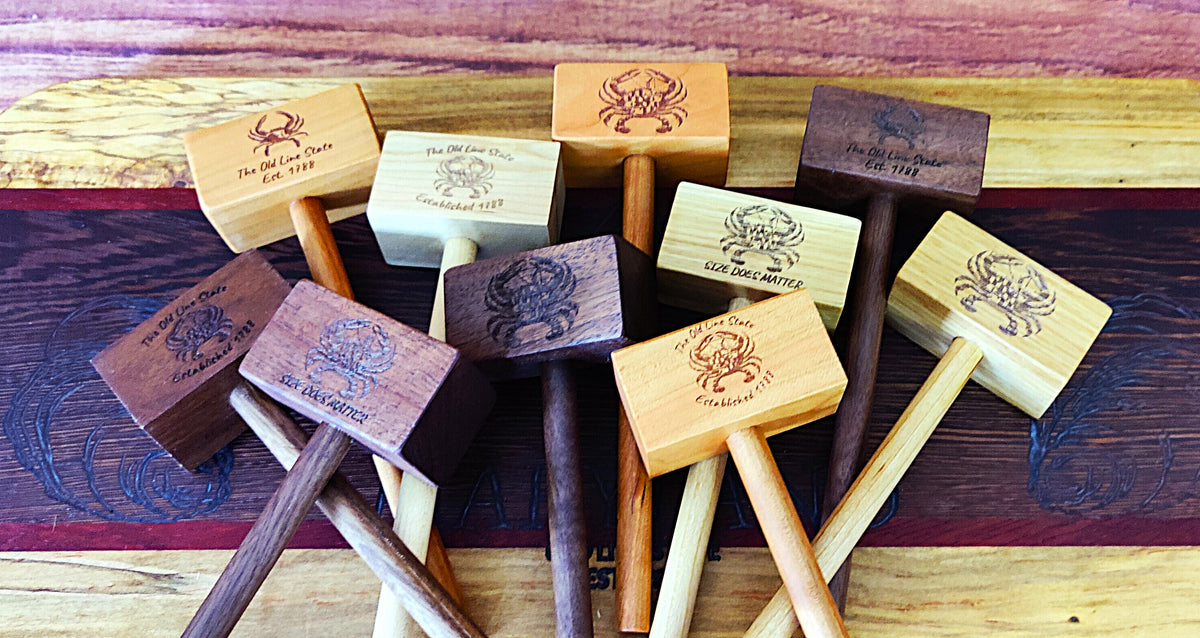 A group of wooden mallet-style tools or hammers arranged on a dark wooden surface, with engraved text and a crab logo visible on several pieces.