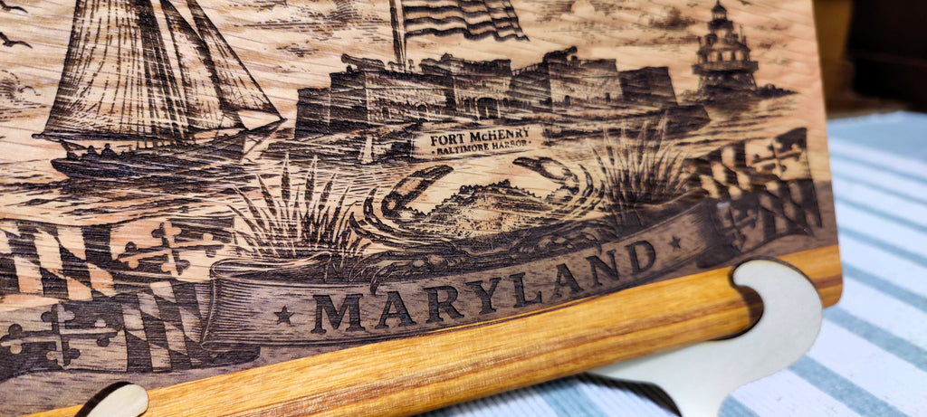 A close-up of a wooden plaque or sign featuring engraved nautical artwork and the word 'MARYLAND' across the front, resting on a striped surface.