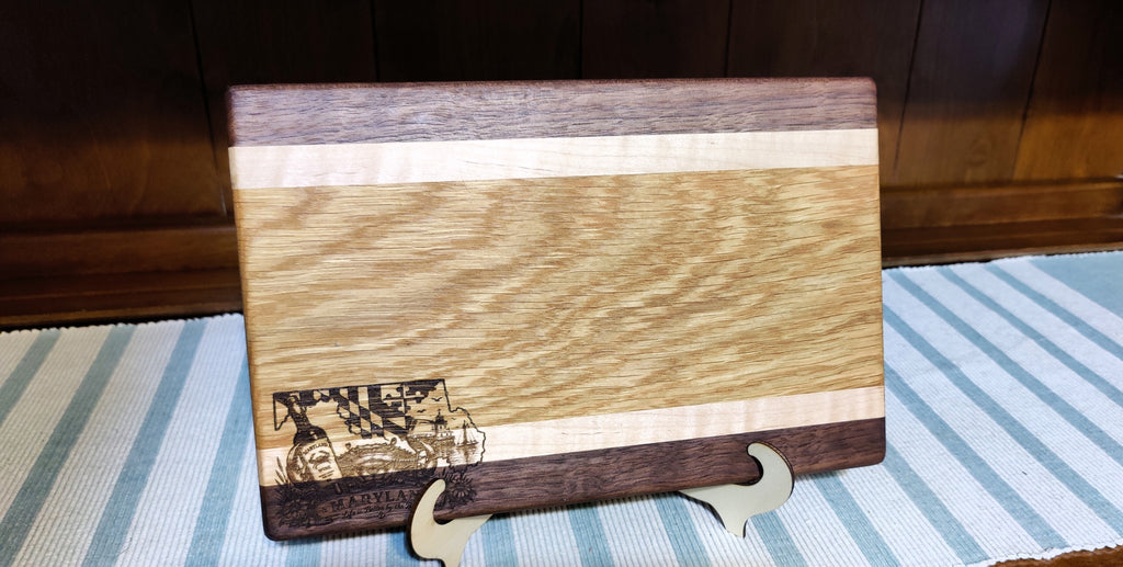 A rectangular wooden cutting board with a striped pattern of light and dark wood, standing on a small wooden display stand on a blue and white striped table runner.
